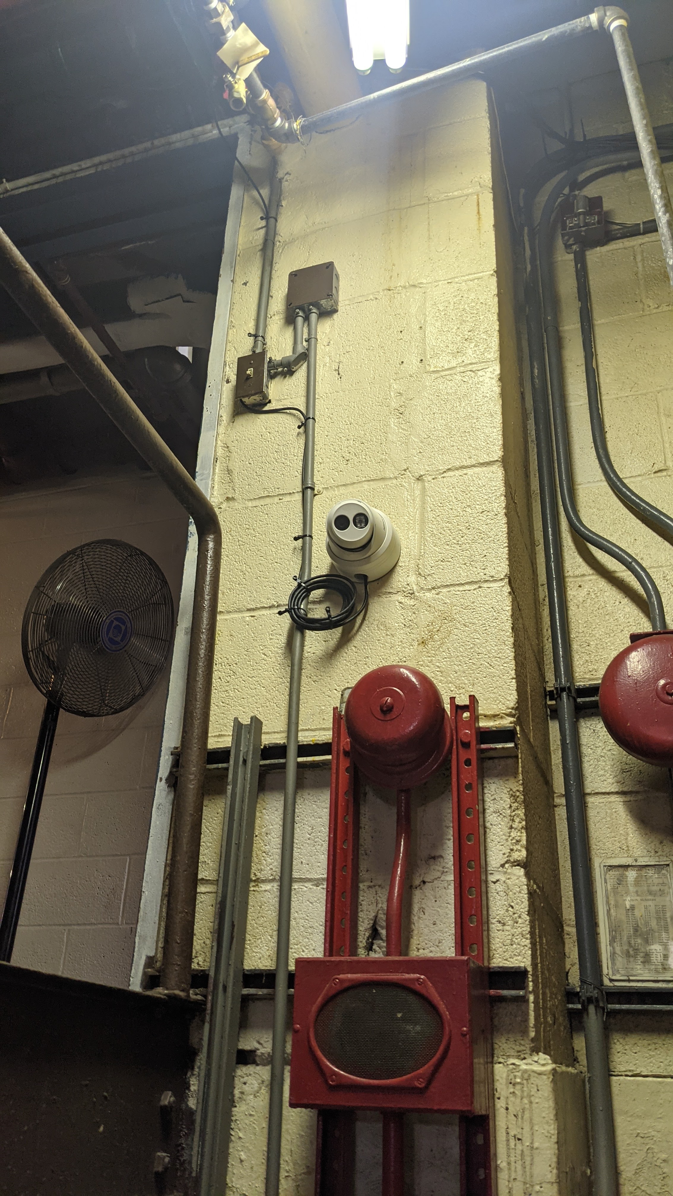 Security camera mounted on a wall near a fire alarm bell in a boiler room