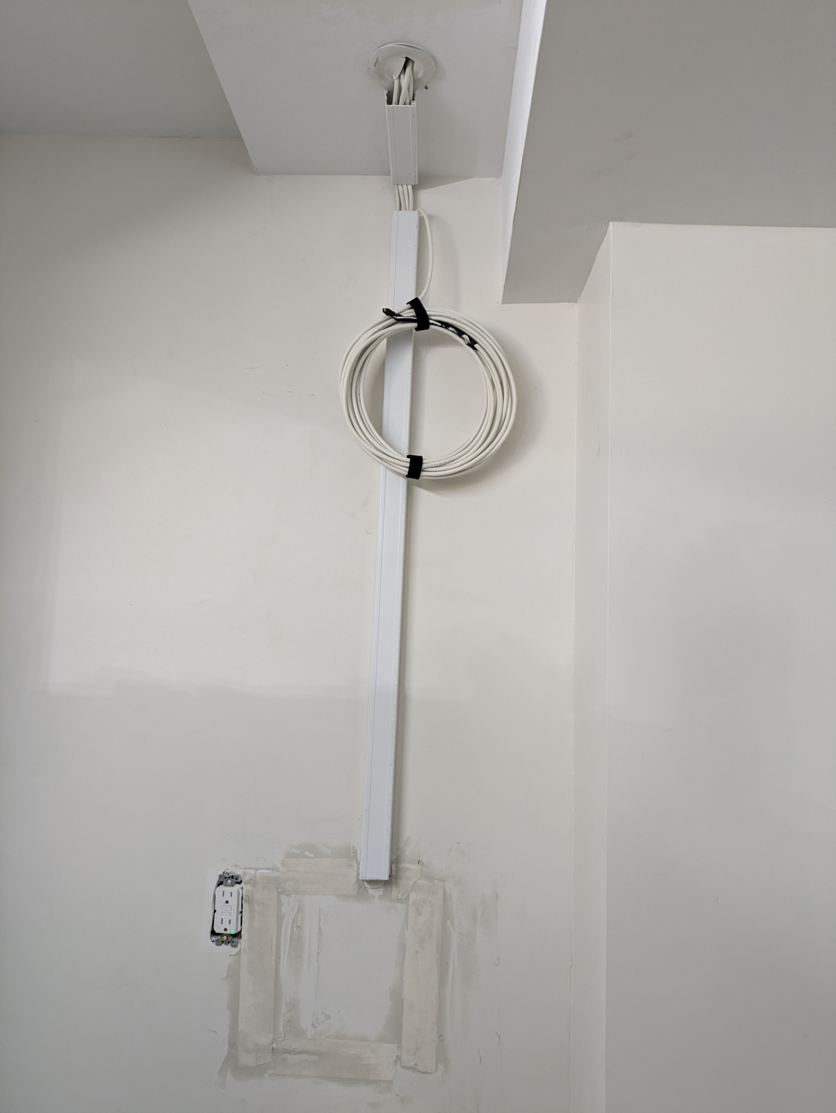 Network cable neatly run up a wall to the ceiling with a coiled service loop